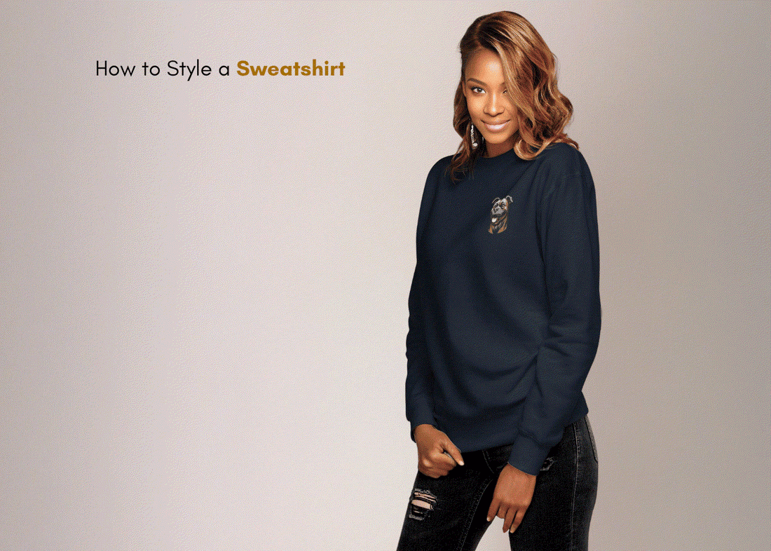 Woman wearing navy blue embroidered sweatshirt styled with black ripped jeans against neutral background with text "How to Style a Sweatshirt"