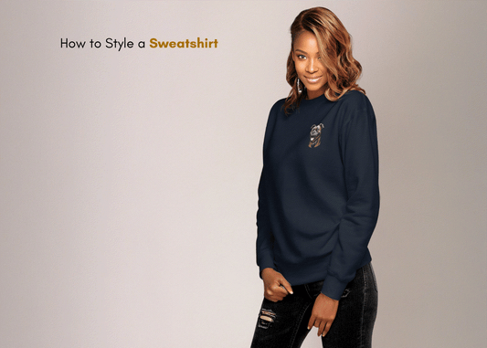 Woman wearing navy blue embroidered sweatshirt styled with black ripped jeans against neutral background with text "How to Style a Sweatshirt"