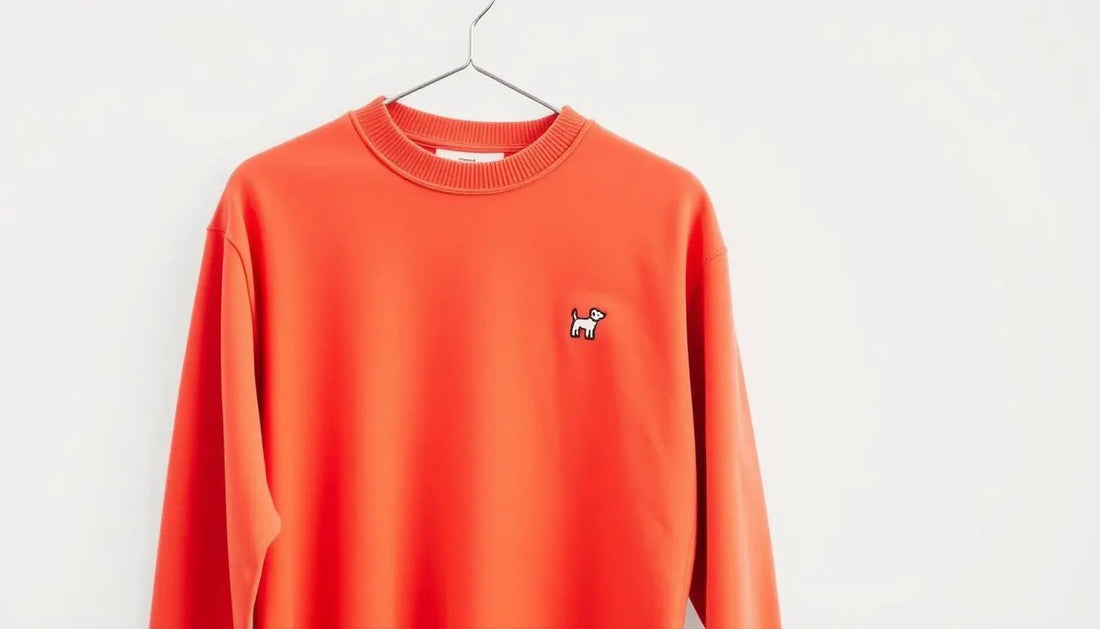 Bright orange basic color sweatshirt with small embroidered dog logo on chest hanging on hanger against white background