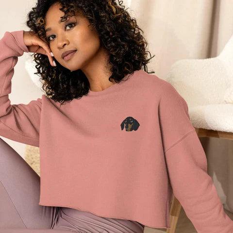 Woman wearing a cozy pink cropped dog-themed sweater with a small dachshund graphic, styled casually indoors.